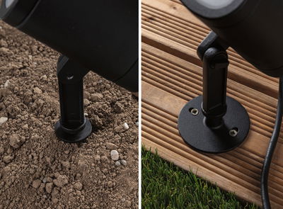 Black metal mount for outdoor spotlight on soil and wooden deck, weatherproof garden lighting fixture.