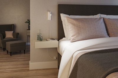 Chambre moderne avec lit rembourré marron, lampe de lecture beige murale et table de chevet flottante en bois.