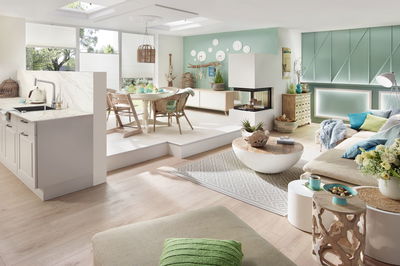 Salon lumineux avec éclairage moderne, murs turquoise, coin canapé confortable et meubles en bois et rotin.