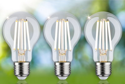 Three clear LED filament bulbs with E27 base against a green and blue blurred background