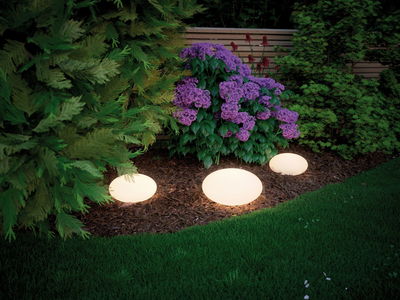 Drie witte LED-tuinkogelverlichting verlichten bloembed met paarse bloemen en groen blad.