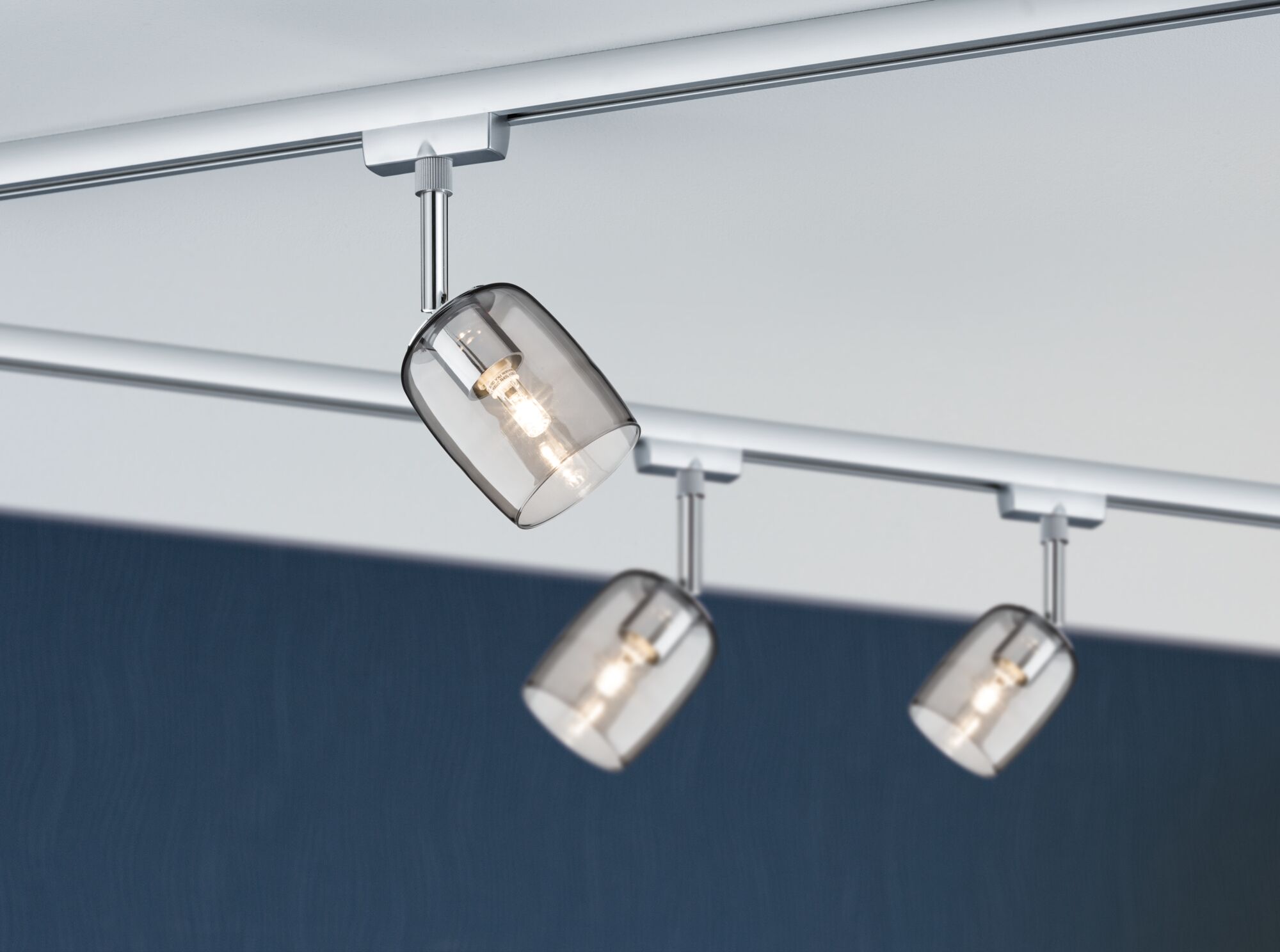 Drei moderne Schienenstrahler mit rauchgrauen Glaslampenschirmen und Chrom-Metall in Wohnraumbeleuchtung