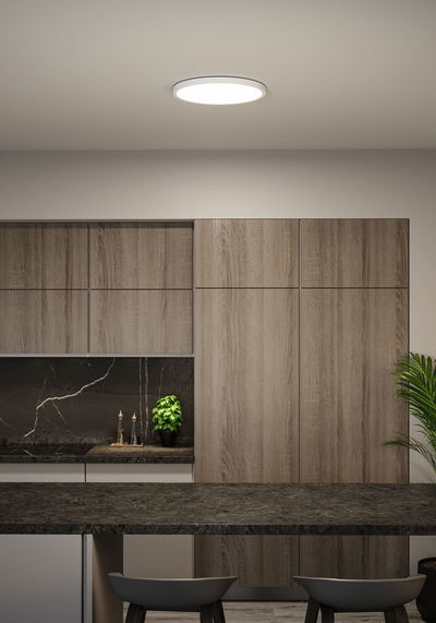 Round white LED ceiling light in modern kitchen with wood cabinets and black countertop