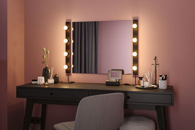 Schwarzer Schminktisch mit Spiegel und warmweißen LED-Leuchten an rosa Wand für Make-up Bereich