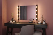 Schwarzer Schminktisch mit Spiegel und warmweißen LED-Leuchten an rosa Wand für Make-up Bereich