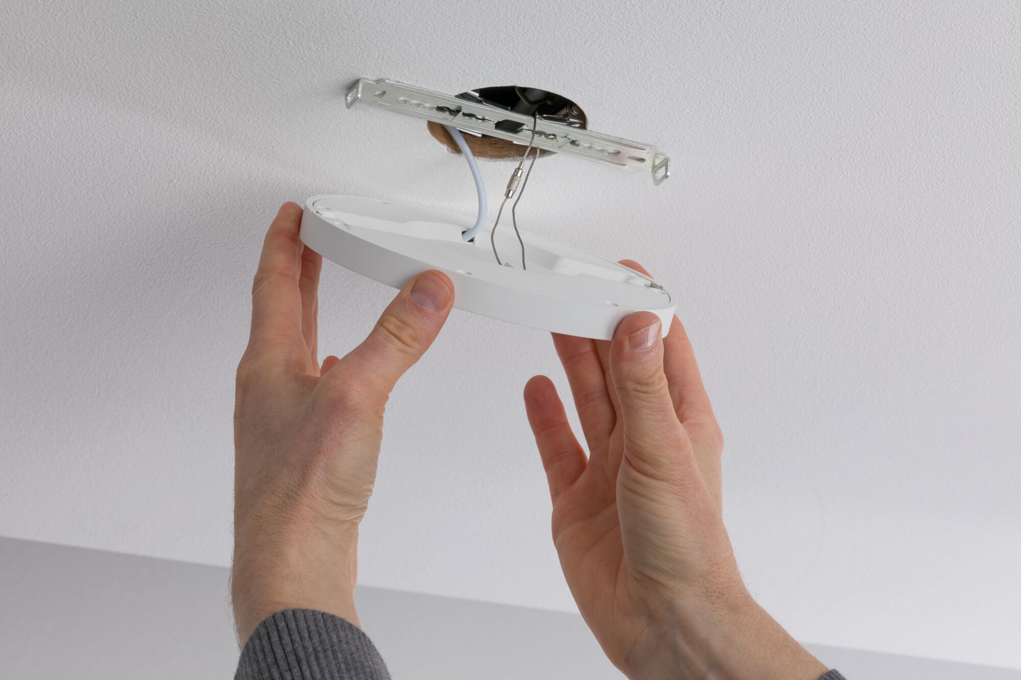 Hands installing white round plastic LED ceiling light on ceiling with metal bracket