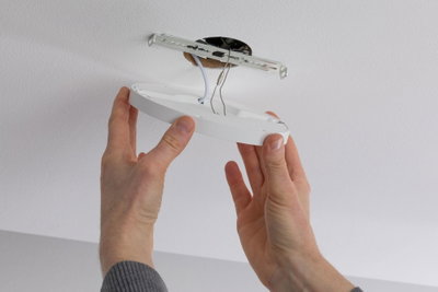 Hands installing white round plastic LED ceiling light on ceiling with metal bracket