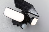 Schwarze Solar-Außenleuchte mit Bewegungsmelder und zwei weißen LED-Leuchtflächen an Wand montiert.