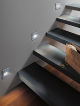 Éclairage LED moderne pour escalier en aluminium argenté avec lumière blanc chaud sur mur gris.