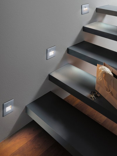 Éclairage LED moderne pour escalier en aluminium argenté avec lumière blanc chaud sur mur gris.