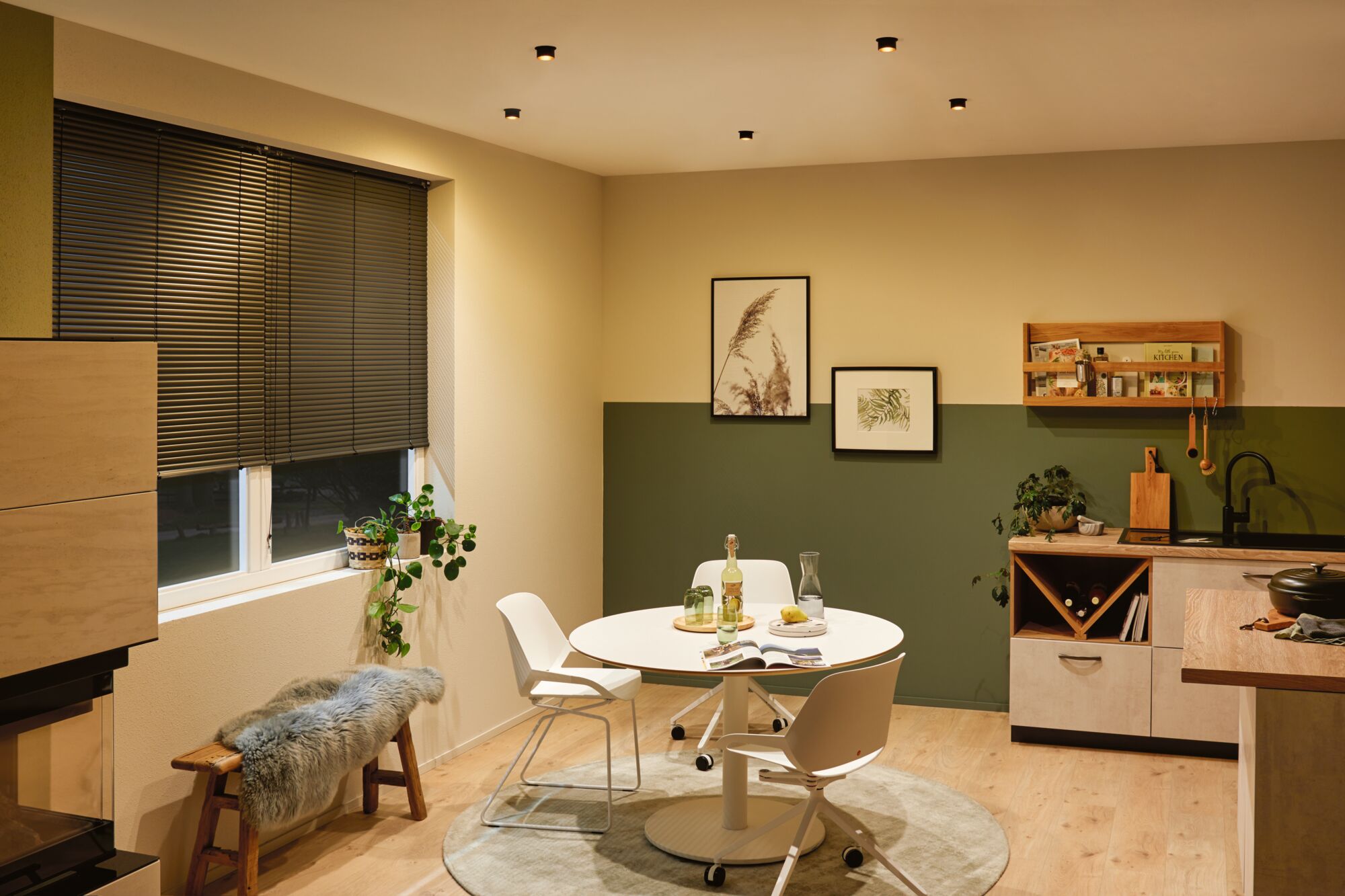 Coin repas moderne avec table ronde blanche, chaises, sol en bois et éclairage mural vert