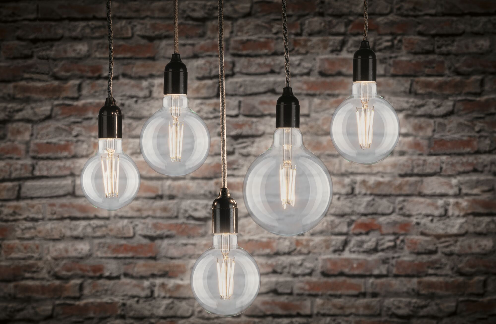 Five clear filament LED bulbs hanging with warm white 2700K light against red brick wall