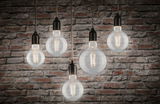 Five clear filament LED bulbs hanging with warm white 2700K light against red brick wall