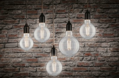 Five clear filament LED bulbs hanging with warm white 2700K light against red brick wall