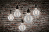 Five clear filament LED bulbs hanging with warm white 2700K light against red brick wall