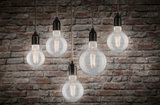 Fünf klare Glühbirnen mit Filament-LEDs vor roter Backsteinwand, warmweißes Licht 2700K
