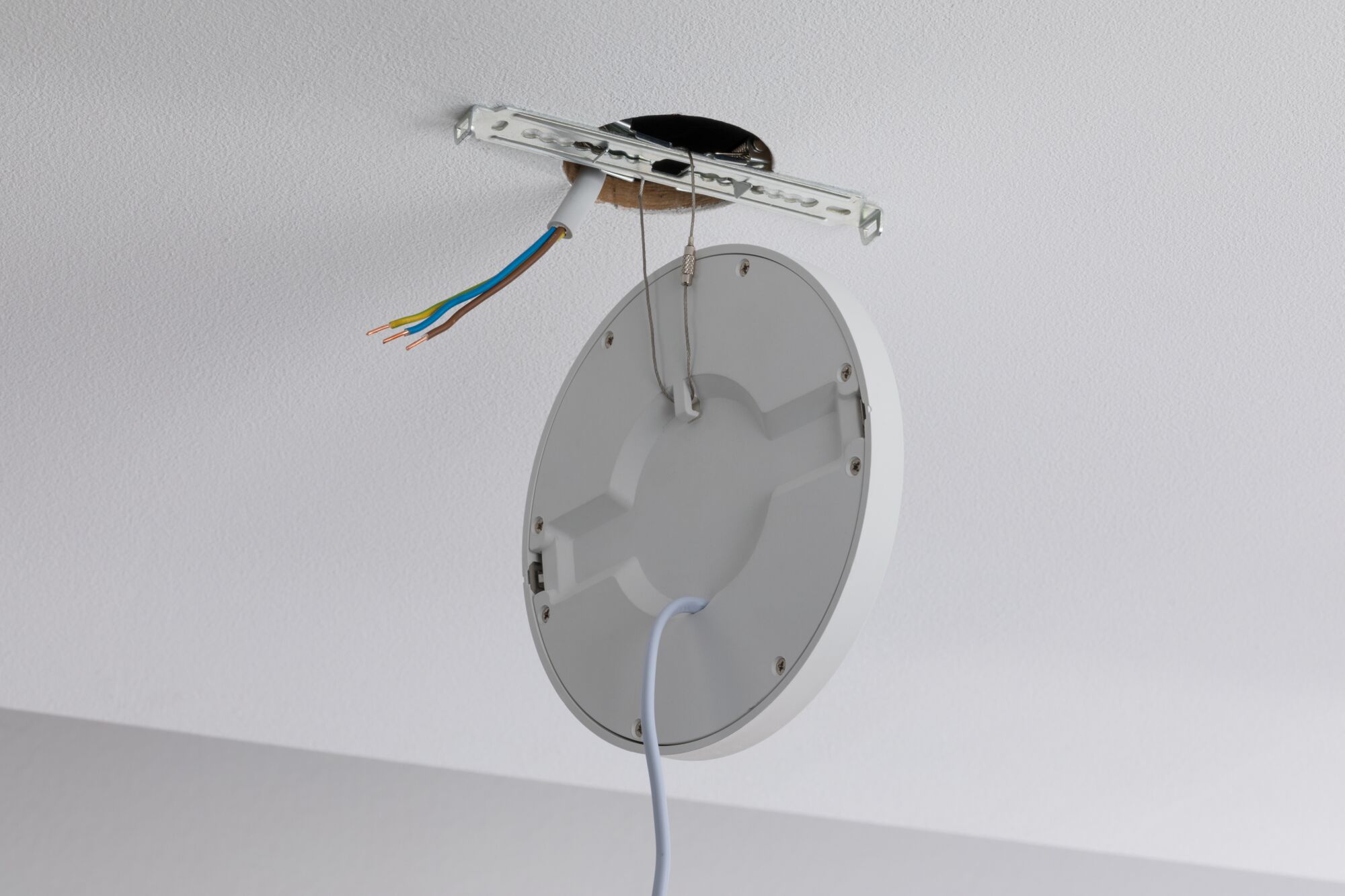 Plafonnier rond blanc en plastique avec câble et fils apparents pour installation.