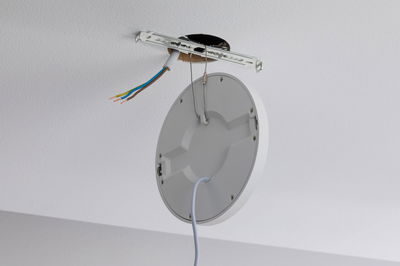 Round white plastic ceiling light with cable and exposed wiring for installation.