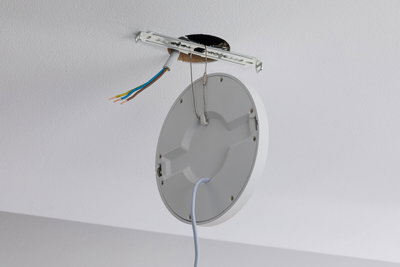 Round white plastic ceiling light with cable and exposed wiring for installation.
