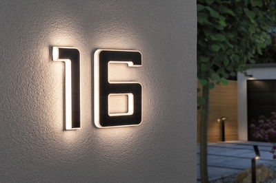 Modern house number 16 in black material with white LED lighting on exterior wall for house number illumination