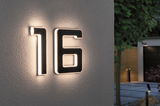 Modern house number 16 in black material with white LED lighting on exterior wall for house number illumination