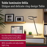 Modern black Odila table lamp with adjustable LED ring on wooden desk in home office setting