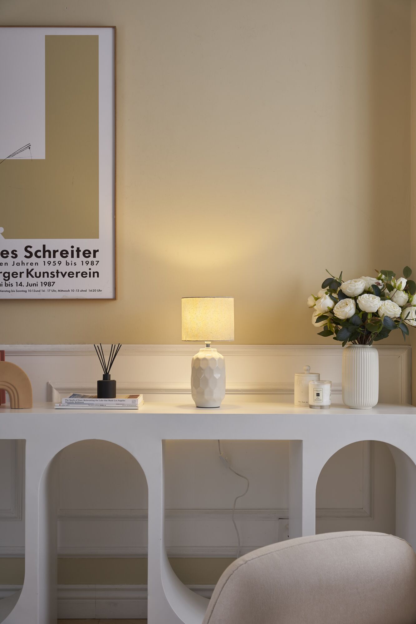 Weiße Keramik-Tischlampe mit strukturiertem Muster und cremefarbenem Lampenschirm auf modernem Sideboard.