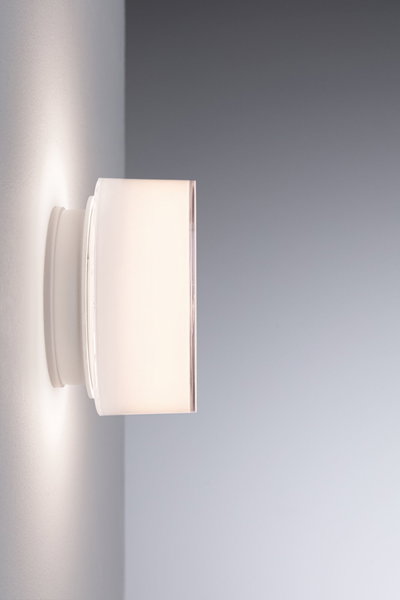 Modern white wall light with cylindrical glass shade emitting soft ambient light