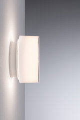 Modern white wall light with cylindrical glass shade emitting soft ambient light