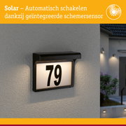 Zwart zonnepaneel huisnummerbord met geïntegreerde schemersensor verlichting aan grijze muur