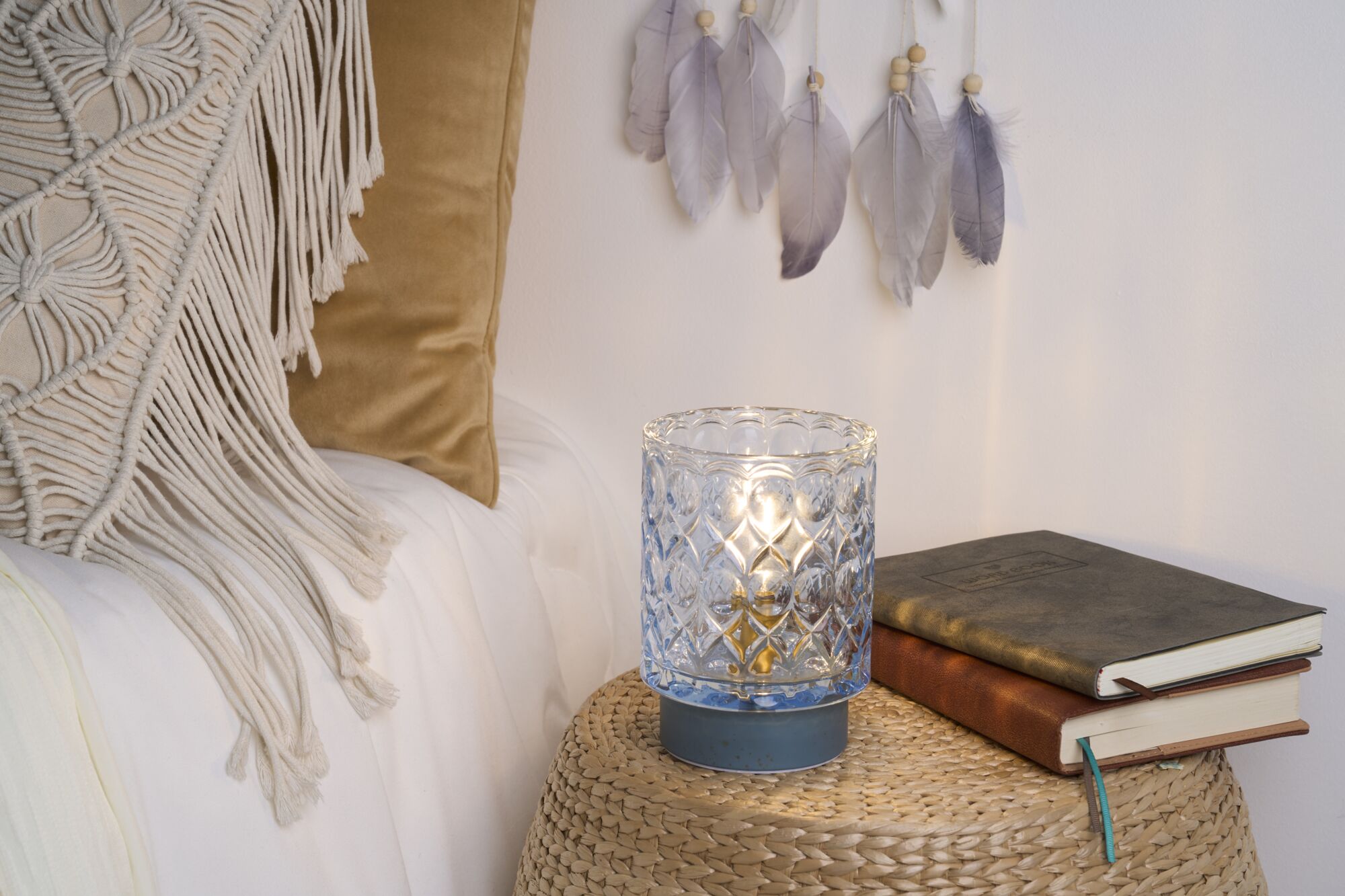 Blue-based glass table lamp with pattern on woven side table next to stacked books for cozy lighting.