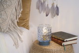 Blue-based glass table lamp with pattern on woven side table next to stacked books for cozy lighting.