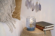 Patterned glass candle holder with blue base on woven table near books and cushions