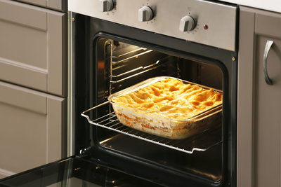Glass baking dish with golden brown casserole inside modern oven in grey kitchen