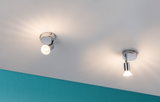 Two chrome LED ceiling spotlights with warm white light on white ceiling and turquoise wall.