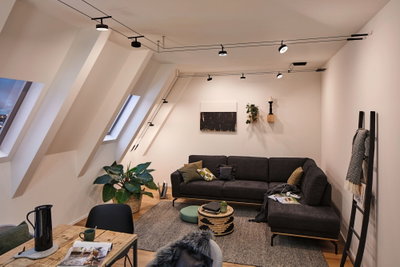 Modernes Wohnzimmer mit schwarzem Ecksofa, grauem Teppich und schwarzer Seilzug-Deckenbeleuchtung für Wohnraum.