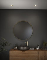 Round bathroom mirror with gold frame above wooden vanity with grey marble sink and gold faucet