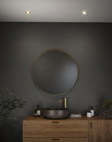 Round bathroom mirror with gold frame above wooden vanity with grey marble sink and gold faucet