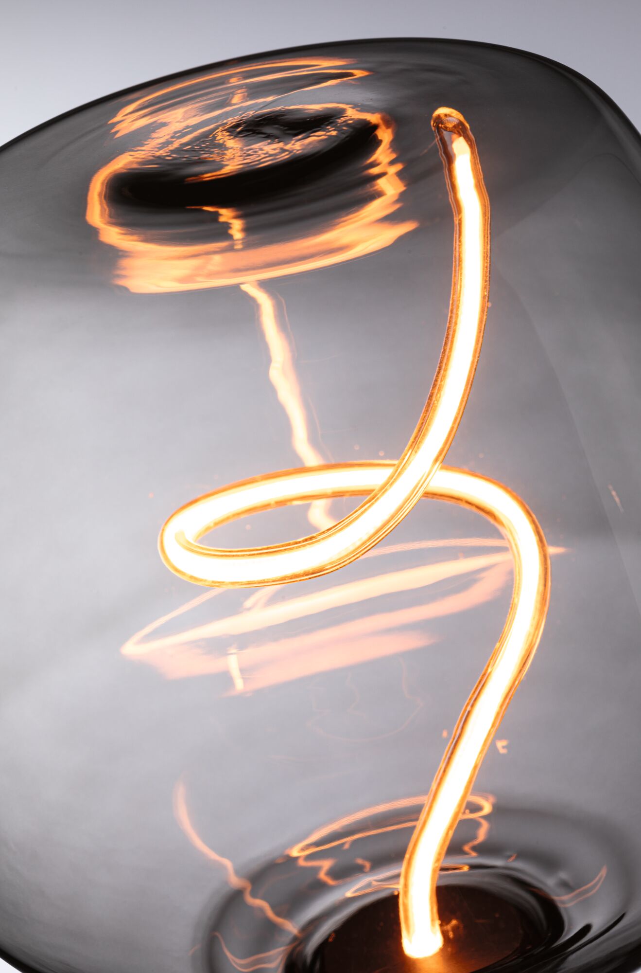 Nahaufnahme einer warm leuchtenden LED-Glühfadenlampe mit geschwungenem Glas in Grau für Wohnraumbeleuchtung