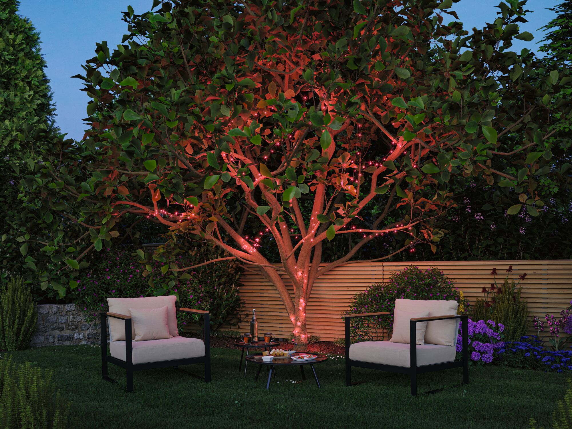 Garten mit Baum, der mit roten LED-Lichterketten beleuchtet ist, umgeben von Sitzmöbeln und Pflanzen