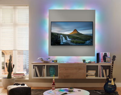 Living room with TV and colorful LED backlight, modern wooden media console and electric guitar
