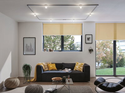 Modernes Wohnzimmer mit schwarzem Sofa, gelben Kissen und Decken, Glas-Couchtisch und gelben Rollos.