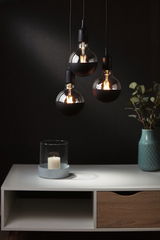 Trois ampoules suspendues avec revêtement noir semi-transparent au-dessus d'une table blanche avec bougie et vase