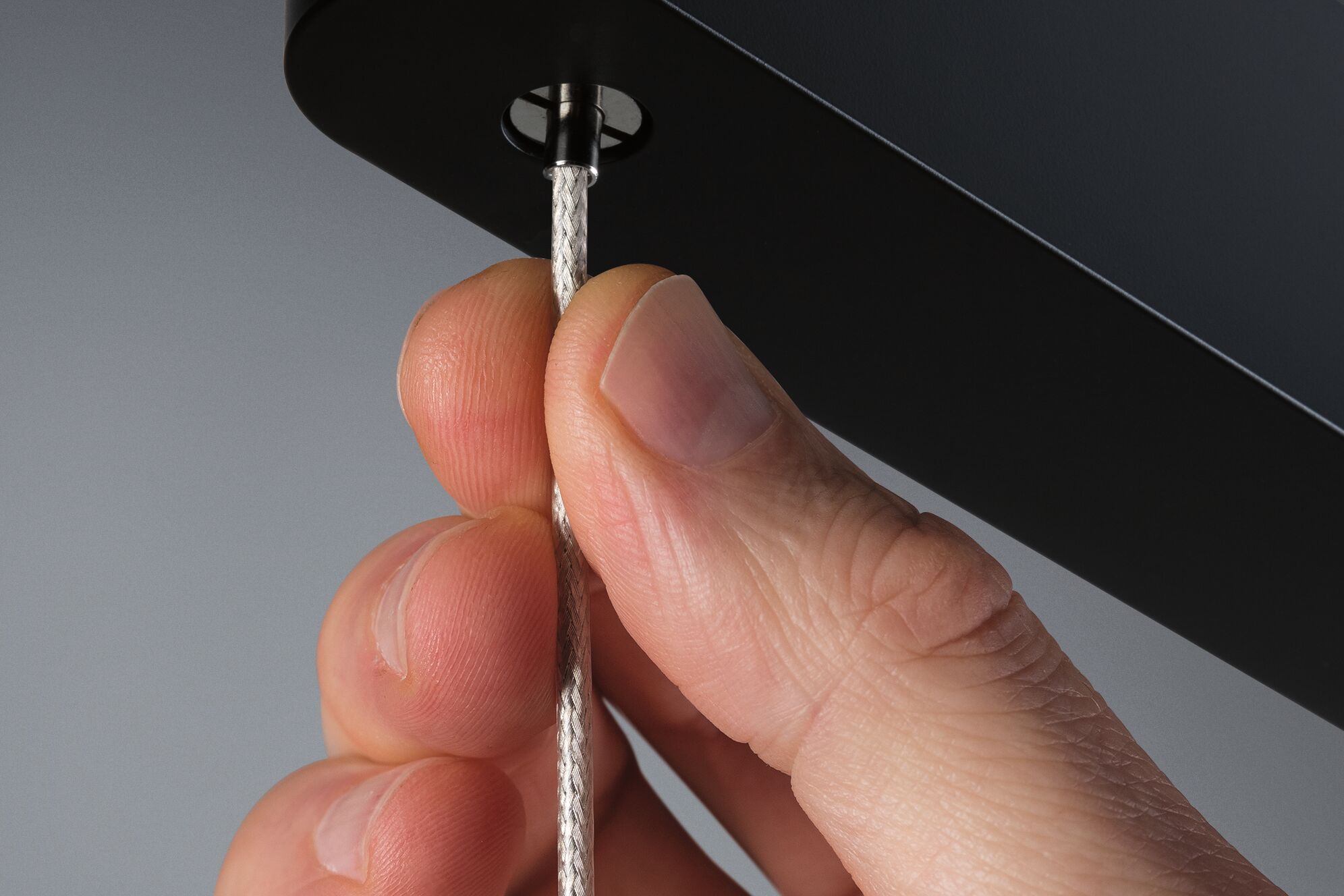 Close-up of hand holding silver textile cable attached to black lighting fixture housing, electrical cable.