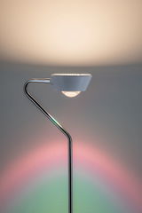 Moderne vloerlamp met witte kap en chromen metalen frame, kleurrijke lichtaccenten op de muur.
