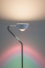 Lampadaire moderne avec abat-jour blanc et structure en métal chromé, accents lumineux colorés sur le mur.