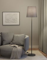 Stehende Stofflampe mit grauem Lampenschirm neben grauem Sessel in modernem Wohnzimmer mit Vorhängen