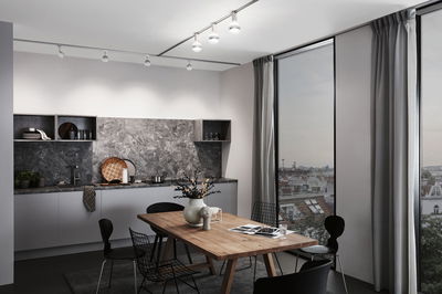 Modernes Esszimmer mit Holz-Tisch, schwarzen Stühlen und grauer Küchenrückwand aus Steinoptik, LED-Deckenstrahler