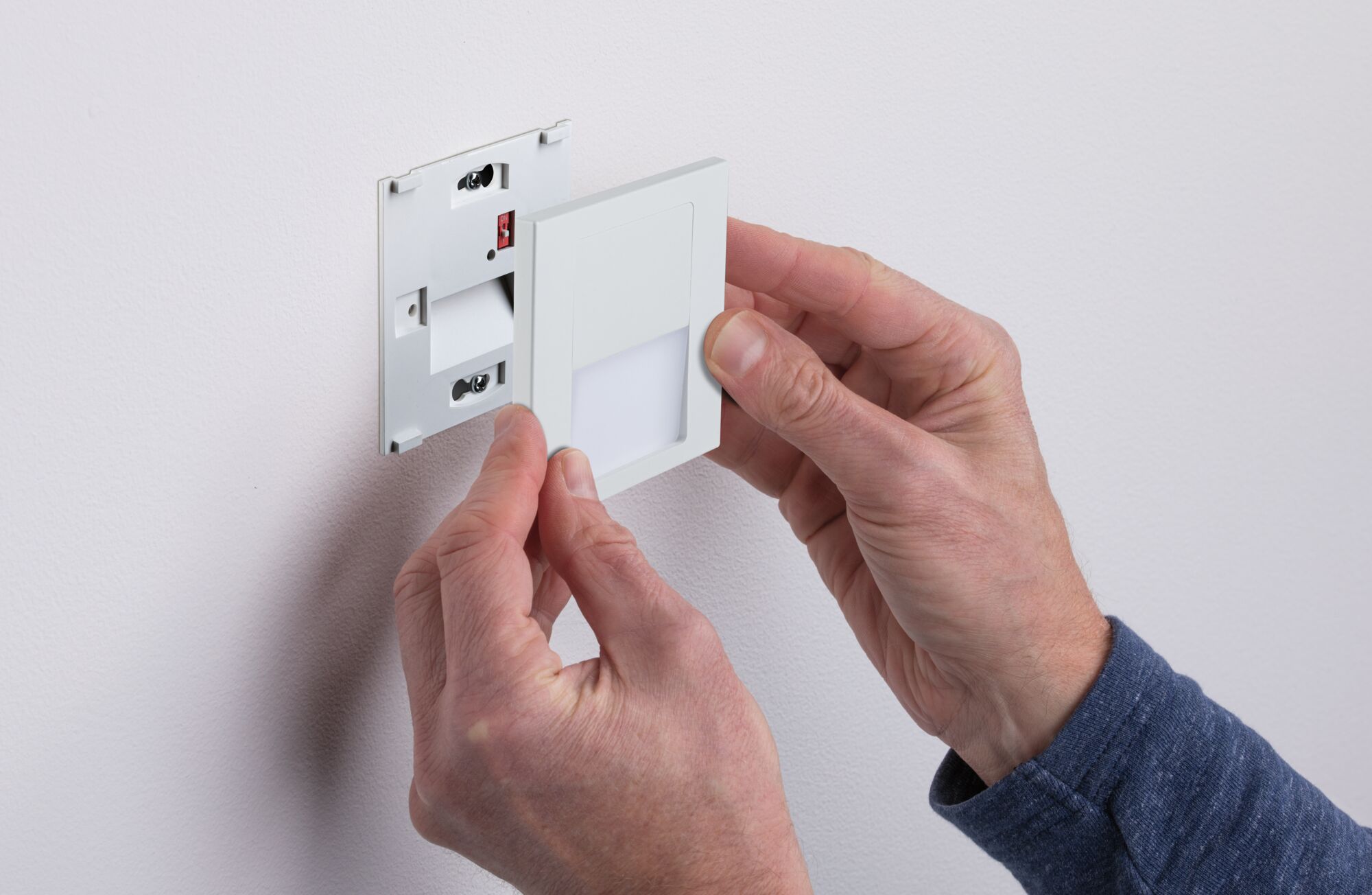 White plastic LED wall recessed light being installed by hands, modern indoor lighting fixture