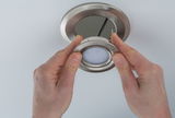 Hands installing round brushed stainless steel recessed spotlight in white ceiling for LED lighting